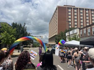 Drag performance at pride festival surrounded by a crowd watching and rainbow backdrop.